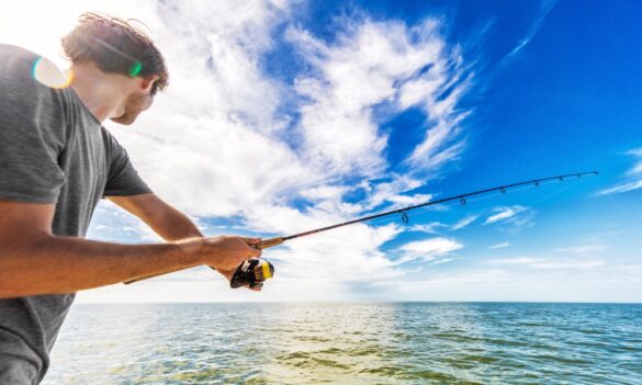 A male is saltwater fishing in the middle of the ocean while actively casting bait and throwing a line.