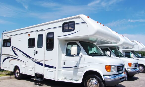 Closeup of a row of several white mid-sized RVs parked outside in a storage parking lot with the sky in the background.
